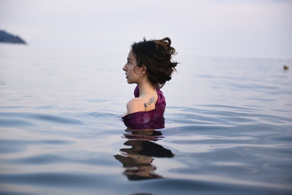 Person submerged to shoulders in cold plunge tub outdoors with steam rising in winter air